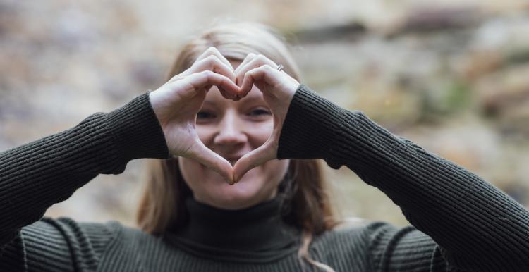 A smiling woman holding up her hands in the shape of a heart