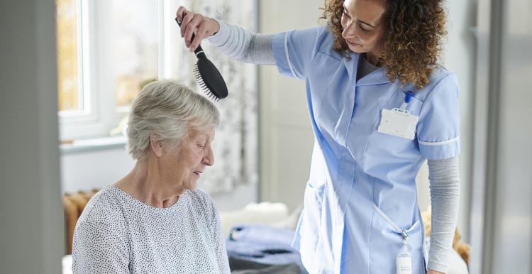 home carer helping older woman get dressed in her bedroom