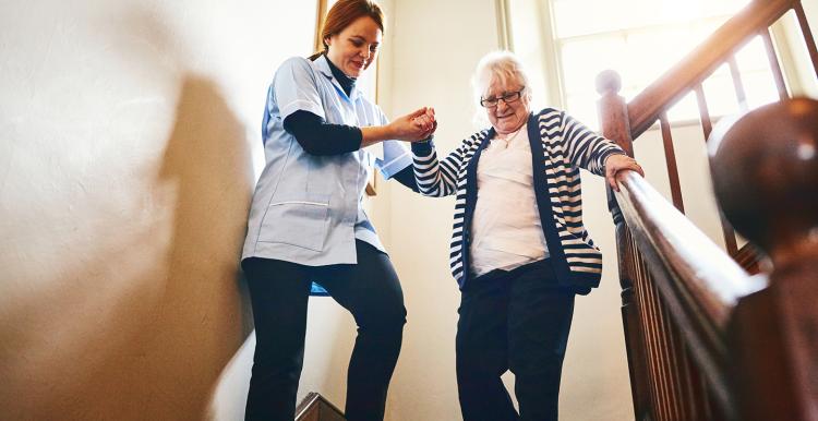Carer helping older woman walking down stairs