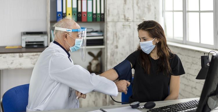 Doctor wearing PPE (personal protective equipment) measures a young woman's blood pressure