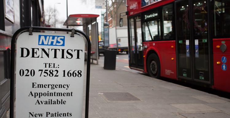 Pre-pandemic photo showing London street with bus stop and NHS dentist sign 