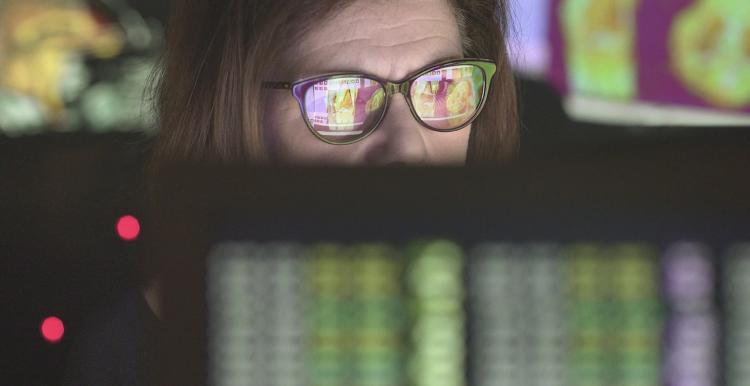 Mature woman intently looking at computer displays. The screens are depicting patient health data. There is a foreground screen showing scrolling numbers