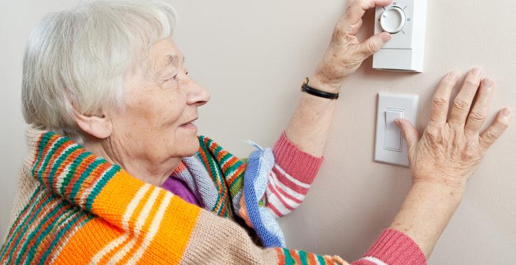 Elderly woman saving energy by dressing warmly and adjusting her thermostat.