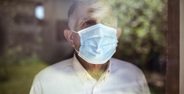 Man wearing a face mask looking out of a window