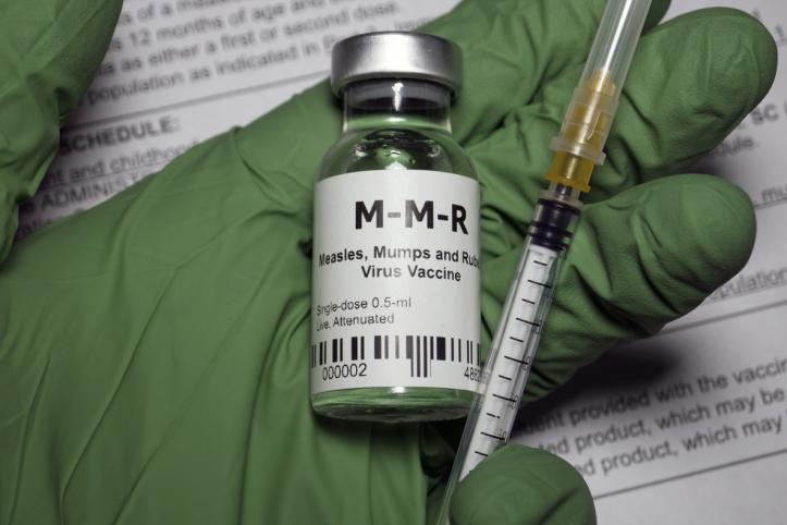 Gloved hand holding MMR vaccine and injection