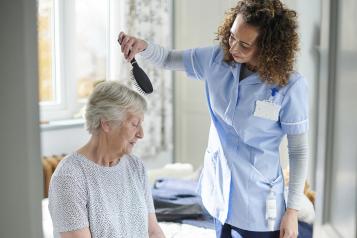 home carer helping older woman get dressed in her bedroom