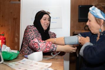 Two women sitting at a table preparing for a blood pressure reading