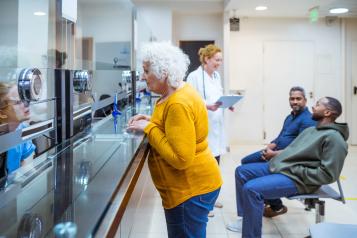 Senior woman talking to a receptionist with a doctor in the background