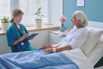 Elderly woman talking with young female doctor in hospital ward
