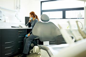 Female dentist sitting at her desk in medical room talking on telephone
