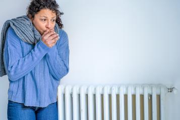 Woman standing next to a radiator trying to keep warm