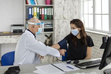 Doctor wearing PPE (personal protective equipment) measures a young woman's blood pressure