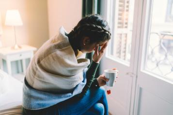 Woman feeling unwell, staying home wrapped in scarf and drinking hot tea