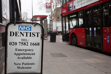 Pre-pandemic photo showing London street with bus stop and NHS dentist sign 