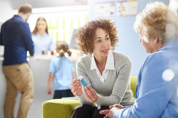 A female pharmacist sits with an older female asthma patient in the pharmacy consultation area and discusses her medication