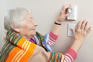 Elderly woman saving energy by dressing warmly and adjusting her thermostat.