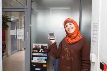 Smiling lady in a headscarf holding up a smartphone