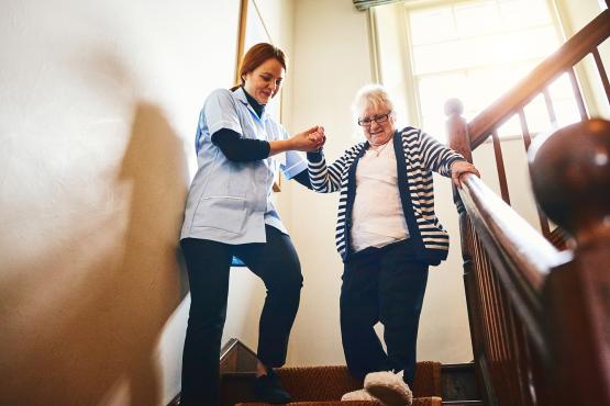 Carer helping older woman walking down stairs