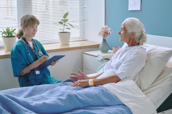 Elderly woman talking with young female doctor in hospital ward
