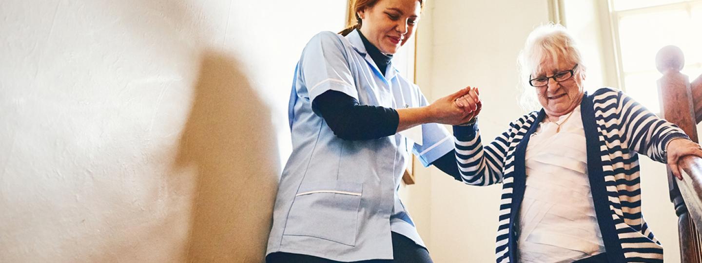 carer helping older woman walking down stairs