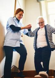 Carer helping older woman walking down stairs